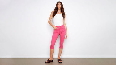 A woman wears pink capri pants styled with a white tank top and dark brown buckle slide sandals.