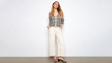 A woman wears a crochet cardigan outfit idea with cream wide-leg pants, black sandals, and a V-neck button front.