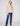 Model wearing beige V-neck long-sleeve top with straight-leg blue jeans and brown ankle boots, posing against light gray background