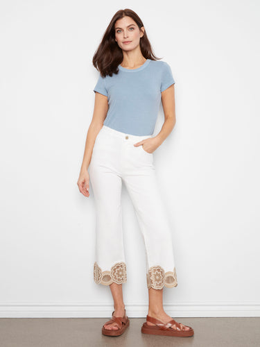 White pants with a flared leg, featuring intricate lace hem detail for added elegance. Crafted from stretch twill fabric by Charlie B.