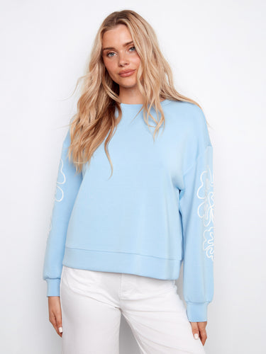 Light blue scuba top with a crew neckline, featuring intricate soutache detailing on the sleeves. Relaxed fit by Charlie B.