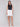 Woman wearing a sleeveless black top paired with a white button-front skirt featuring a scalloped hem, styled with beige slide sandals, on grey background.