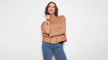  Woman wearing a camel suede bomber jacket over a black top, paired with medium-wash jeans.