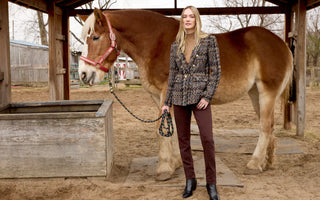Certainly! Here’s the revised alt text incorporating **“tailored blazer”**:  **Alt text:** *Woman standing beside a large brown horse in a stable, wearing a tailored patterned blazer, brown pants, black ankle boots.