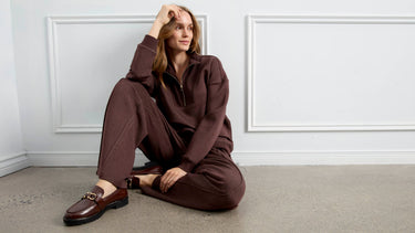 A woman wearing a brown zip-neck sweatshirt and matching sweatpants, seated on the floor.