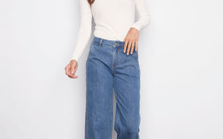 A woman wearing wide-leg blue jeans demonstrates how to wash jeans and care for denim properly