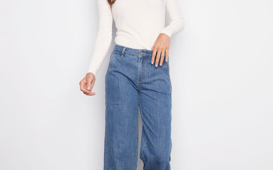 A woman wearing wide-leg blue jeans demonstrates how to wash jeans and care for denim properly