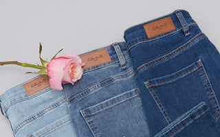 Pair of Charlie B blue jeans with a pink rose on a light gray background
