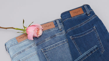 Pair of Charlie B blue jeans with a pink rose on a light gray background