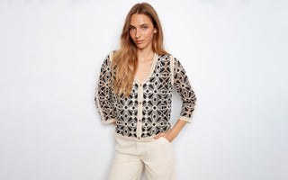 A woman wears a black and off-white crochet cardigan.