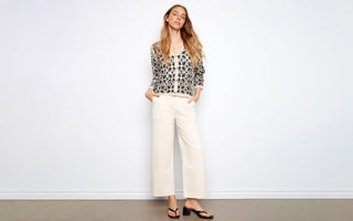 A woman wears a crochet cardigan outfit idea with cream wide-leg pants, black sandals, and a V-neck button front.