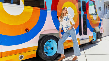 Blonde model in a white floral-embroidered sweater and light-wash flare jeans from Charlie B, styled with brown loafers.