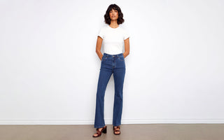 A woman wears women's indigo jeans in a bootcut style, paired with a white tee and brown block-heel sandals.