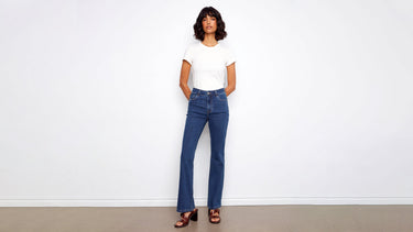 A woman wears women's indigo jeans in a bootcut style, paired with a white tee and brown block-heel sandals.