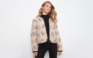 A woman wearing a floral-embroidered quilted jacket with navy trim 