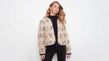 A woman wearing a floral-embroidered quilted jacket with navy trim 