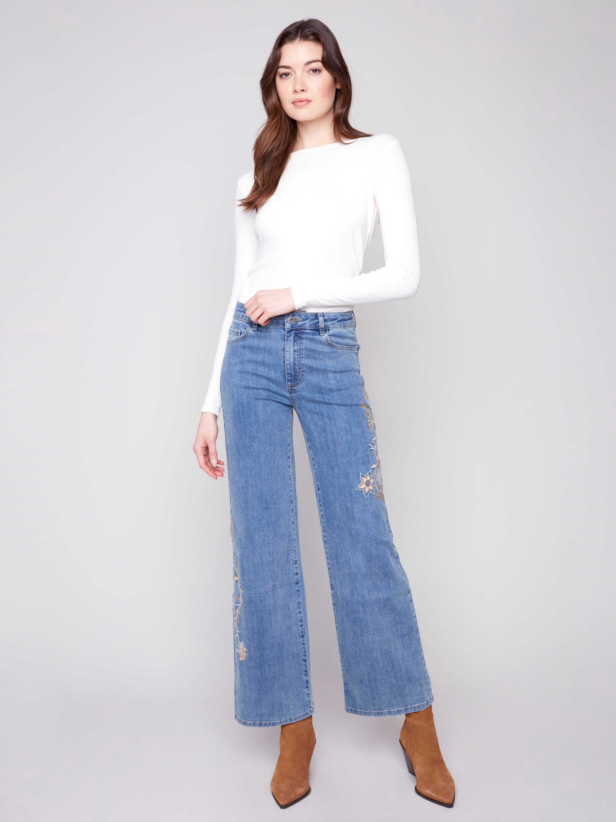 Blue jeans featuring a long length with intricate floral embroidery and sequins by Charlie B.