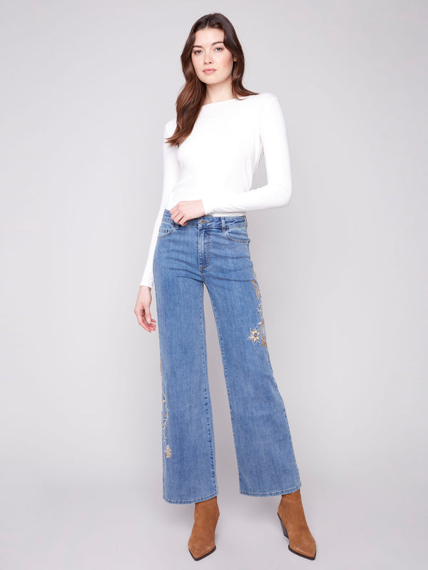 Blue jeans featuring a long length with intricate floral embroidery and sequins by Charlie B.
