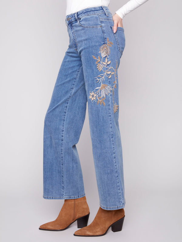 Denim pants with a five-pocket design, showcasing floral embroidery details by Charlie B.