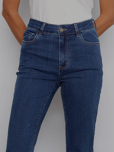 A woman wearing mid-wash bootcut jeans, a white fitted tee, and brown block heels. 
