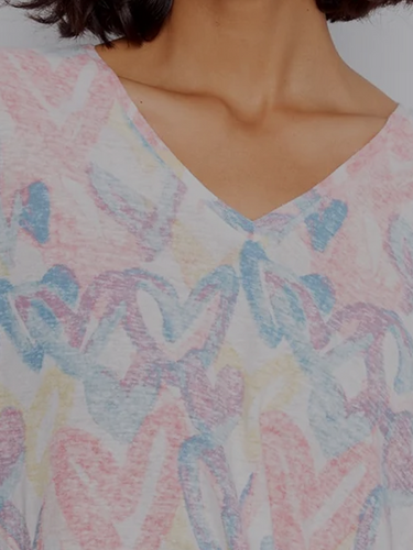 A woman wearing a V-neck top outfit in a pastel heart print with short sleeves, paired with white straight-leg pants.