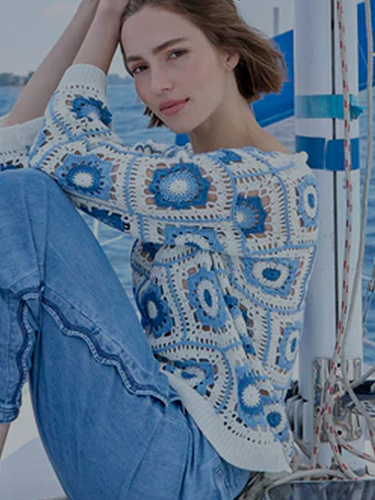    Woman reclining on the floor wearing dark blue bootcut jeans, a white short-sleeve t-shirt, and tan leather loafers with gold horsebit detail, against a plain grey studio background.