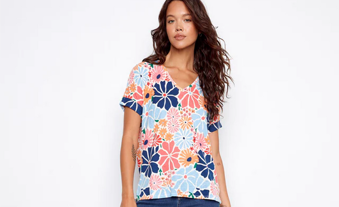 A woman wearing a V-neck top in a bold retro floral print with mid-wash bootcut jeans and brown block heel sandals.