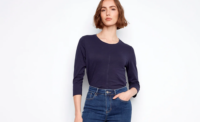 A woman wearing high-rise dark-wash skinny jeans, a navy three-quarter-sleeve top, and brown heeled sandals.
