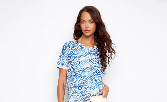 A woman wearing a V-neck top in a blue geometric print with cream wide-leg cropped pants and white strappy sandals.