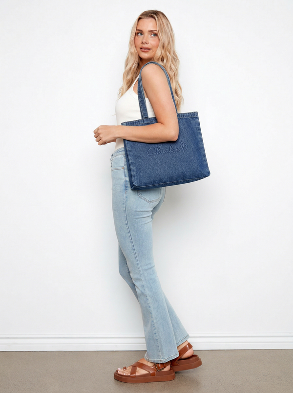 Model showcasing a denim tote bag with a length of 16 inches. Perfect blend of fashion and function by Charlie B.