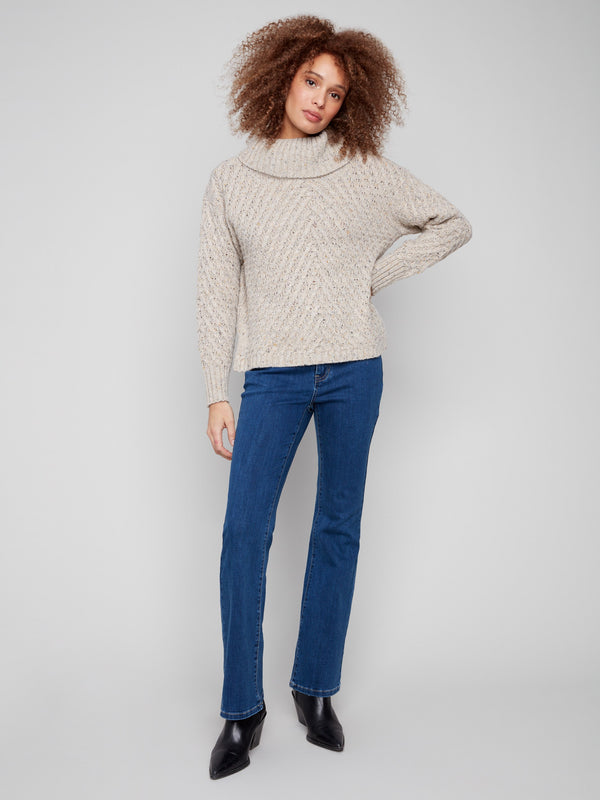 Oat-colored sweater showcasing a relaxed fit with intricate diagonal cable patterns and ribbed detailing by Charlie B.