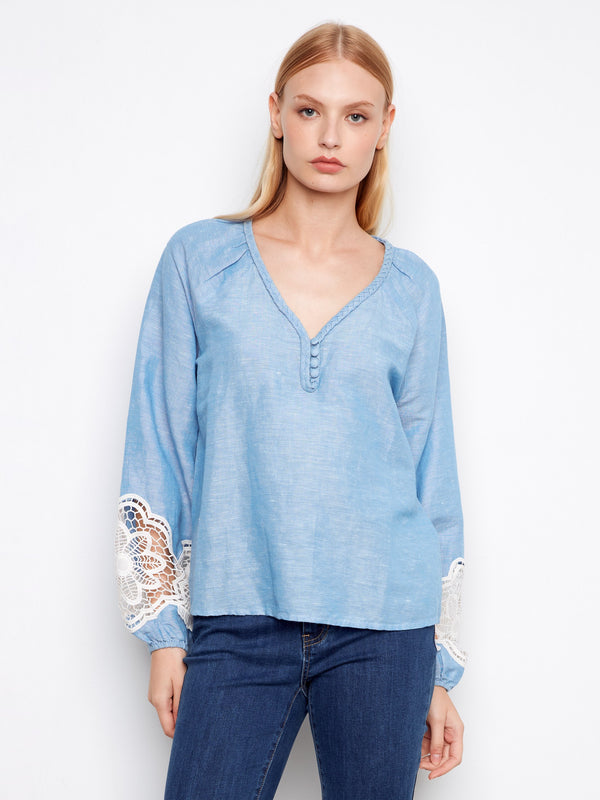 Blue blouse featuring a braided V-neck design, paired with jeans for a stylish look. By Charlie B.