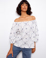 White off-the-shoulder top with delicate floral embroidery, featuring 3/4 sleeves for a chic look. Crafted from 100% cotton by Charlie B.