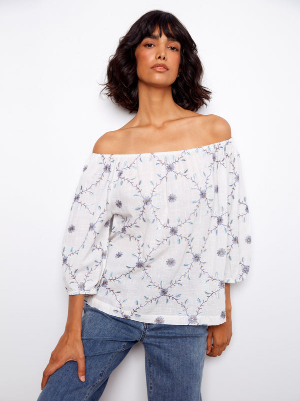 White off-the-shoulder top with delicate floral embroidery, featuring 3/4 sleeves for a chic look. Crafted from 100% cotton by Charlie B.