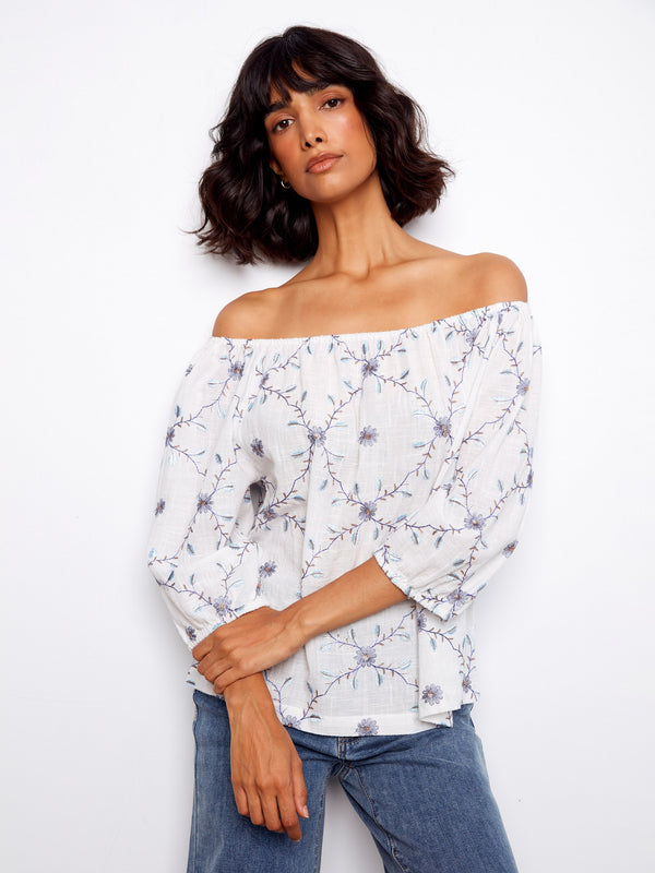 Chic white blouse showcasing exquisite floral embroidery and an elegant off-the-shoulder design. Made from 100% cotton by Charlie B.
