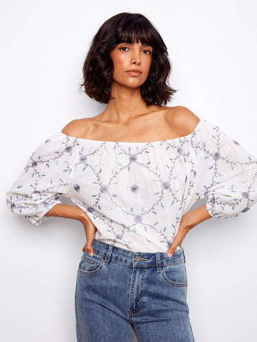 Elegant white top highlighting a beautiful floral pattern with an off-the-shoulder style and comfortable 3/4 sleeves by Charlie B.