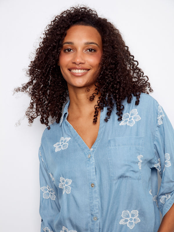 Stylish light blue blouse adorned with floral embroidery, showcasing a chic front tie detail by Charlie B.