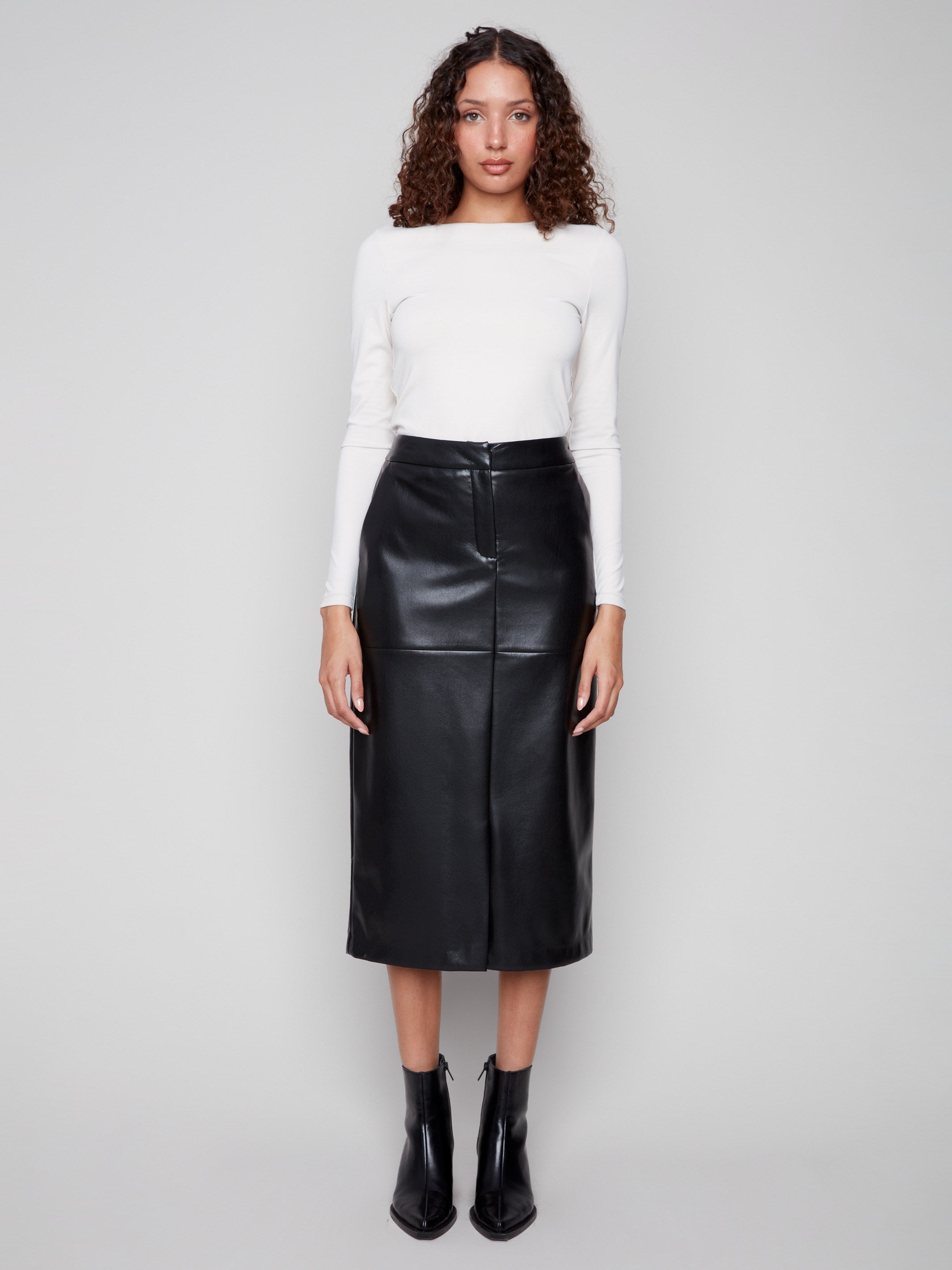 Sophisticated black faux leather skirt showcasing its midi length, combined with a crisp white top and stylish boots by Charlie B.