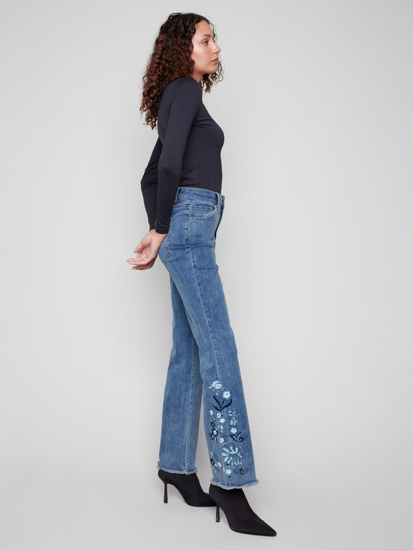 Blue flared jeans featuring a long length and intricate floral designs along the sides by Charlie B.