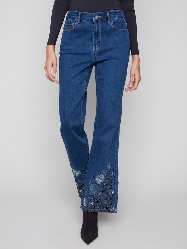 These long indigo jeans feature intricate floral lace at the hem, paired with a classic five-pocket style by Charlie B.