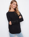 Black knit sweater with a boat neckline and rounded hem, featuring stylish lace-up cuffs and practical side pockets by Charlie B.