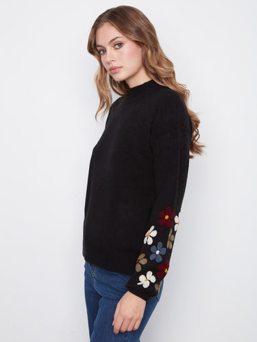 Elegant black sweater showcasing a mock neckline and colorful embroidered flowers on the sleeves by Charlie B.