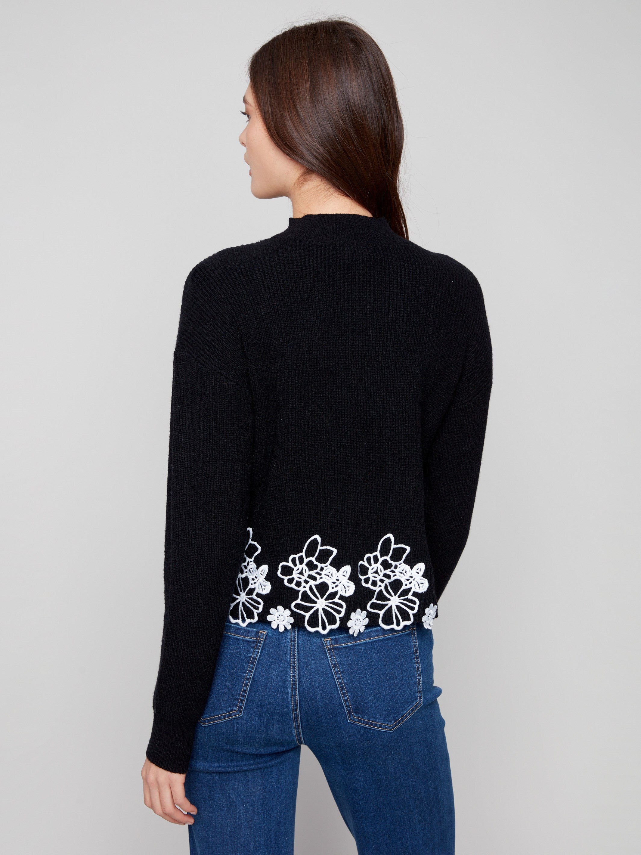 Stylish black sweater showcasing a drop shoulder design and intricate white floral lace accents at the hem by Charlie B.