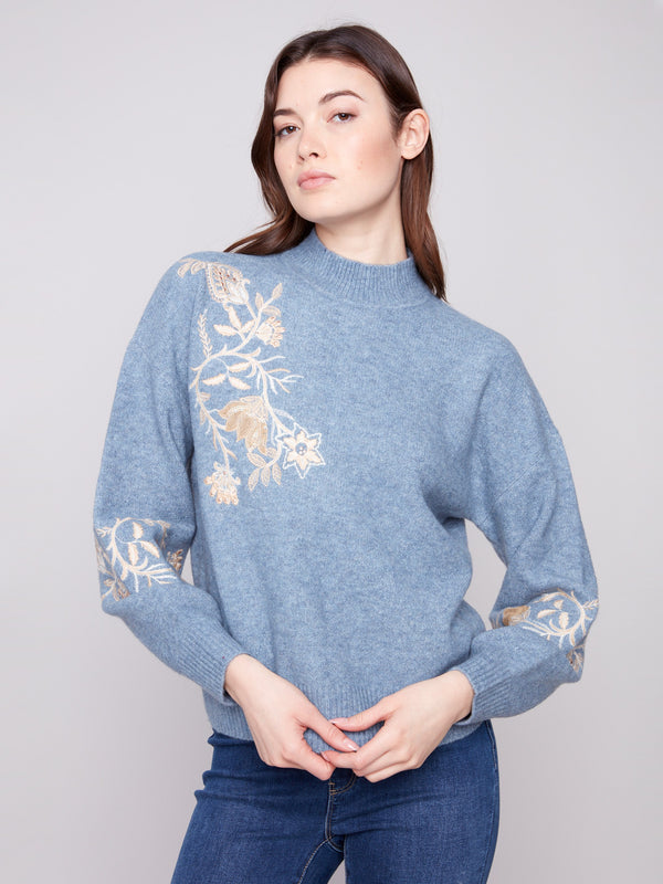 Elegant heather denim sweater adorned with delicate embroidered flowers and shimmering sequins, complete with drop shoulders by Charlie B.