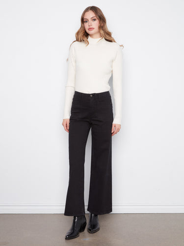 Black wide-leg pants in stretch twill fabric, paired with black boots and a white sweater by Charlie B.