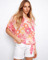 Model in a floral printed blouse with short dolman sleeves, styled with white shorts by Charlie B.