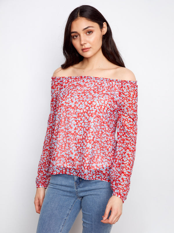 Elegant red blouse with a floral design, featuring an off-the-shoulder neckline and balloon sleeves. Styled with jeans by Charlie B.
