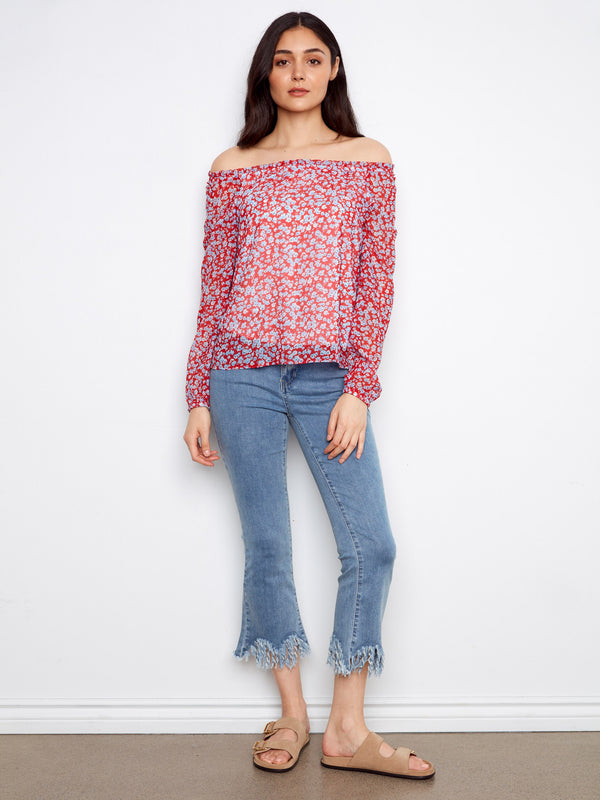 Chic floral blouse in red, showcasing elastic cuffs and an off-the-shoulder design. Paired with frayed hem jeans by Charlie B.