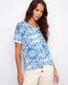 Blue patterned top with a V-neckline, paired with beige pants. Features short sleeves for a relaxed look by Charlie B.