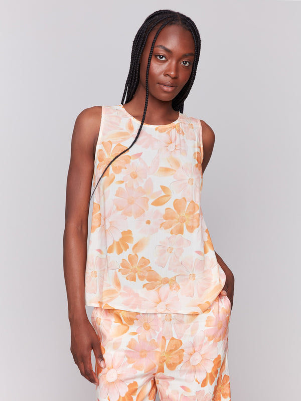 Woman wearing a sleeveless top and matching pants with an all-over peach and orange floral print, standing against a plain light grey background.